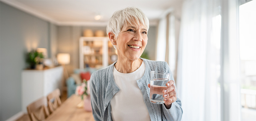 A senior woman smiling and holding a glass of water.